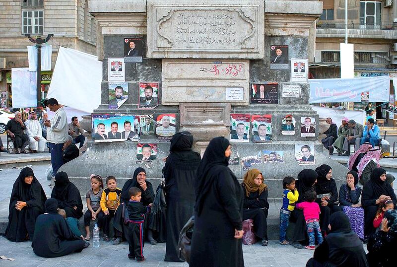 Syrians sit in front of campaign posters for parliamentary candidates in Damascus' Marjeh square on April 11, 2016. The government’s insistence on holding its own parliamentary elections could be perceived as a sign of ill will by the opposition and cause friction in Geneva. Hassan Ammar/AP Photo
