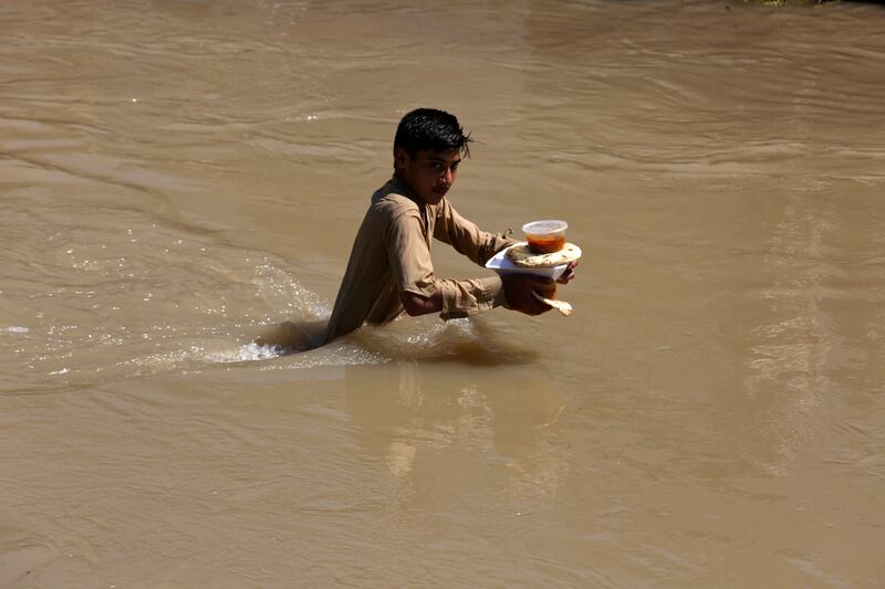 A displaced boy who fled his flood-hit home carries food rations as he wades through water. AP Photo