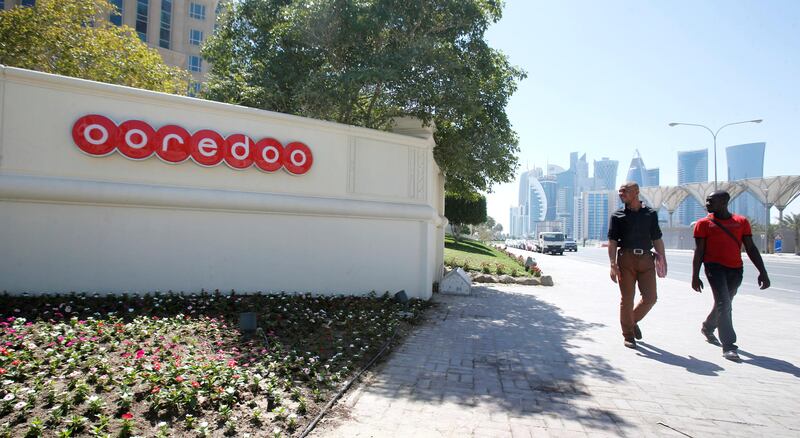 FILE PHOTO: Men look at the logo of Qatar Telecom Ooredoo, formerly Qatar Telecom Qtel, as they walk past the company's head office in Doha March 16, 2013.  REUTERS/Fadi Al-Assaad/File Photo         GLOBAL BUSINESS WEEK AHEAD      SEARCH GLOBAL BUSINESS 24 JUL FOR ALL IMAGES