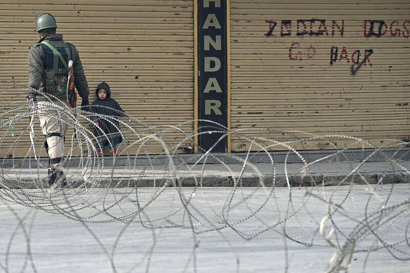 An Indian paramilitary trooper closes a barbed fence wire as a Kashmiri child looks on during a restriction by government forces in Srinagar on January 28, 2018.
Authorities have impose restrictions in parts of Srinagar in view of the strike call issued by the joint resistance leadership (JRL) against the civilian killings in Kashmir. / AFP PHOTO / TAUSEEF MUSTAFA