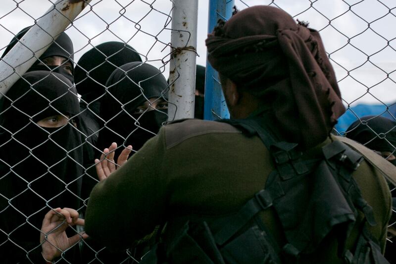 In this March 31, 2019, photo, women speak to guards at the gate that closes off the section for foreign families who lived in the Islamic State's so-called caliphate, at al-Hol camp in Hasakeh province, Syria.  As Turkish troops invade northern Syria and the U.S. abandons its Kurdish allies, there are renewed fears of a prison break in the camp that could give new life to the extremist group.  (AP Photo/Maya Alleruzzo)