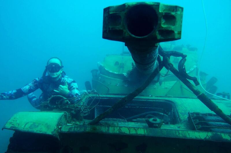 A diver poses next to the a sunk tank.