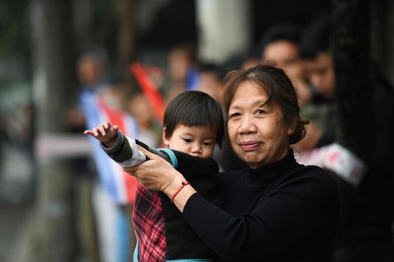 A woman and a child wave as Kim Jong-un's motorcade drives past in Hanoi. AFP