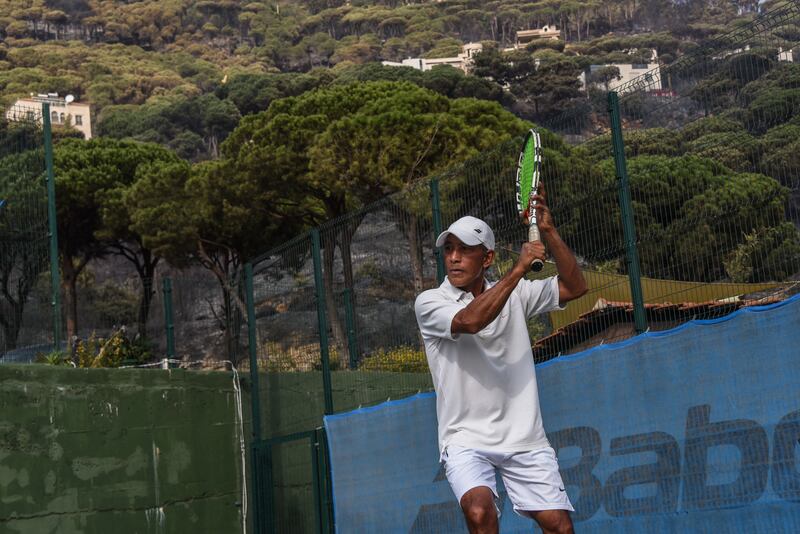 Coach Marco Villiegas plays tennis at the Overhead Tennis Academy against a charred backdrop.