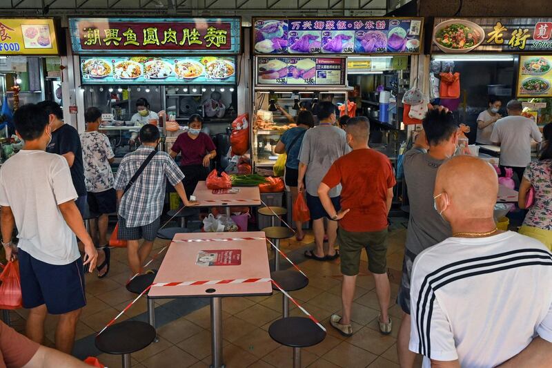 People queue to buy takeaway meals, as tables and chairs are cordoned off to prevent people from dining, at a hawker food centre in Singapore, on the first day of increased restrictions over concerns in a rise in the number of Covid-19 coronavirus cases.   AFP