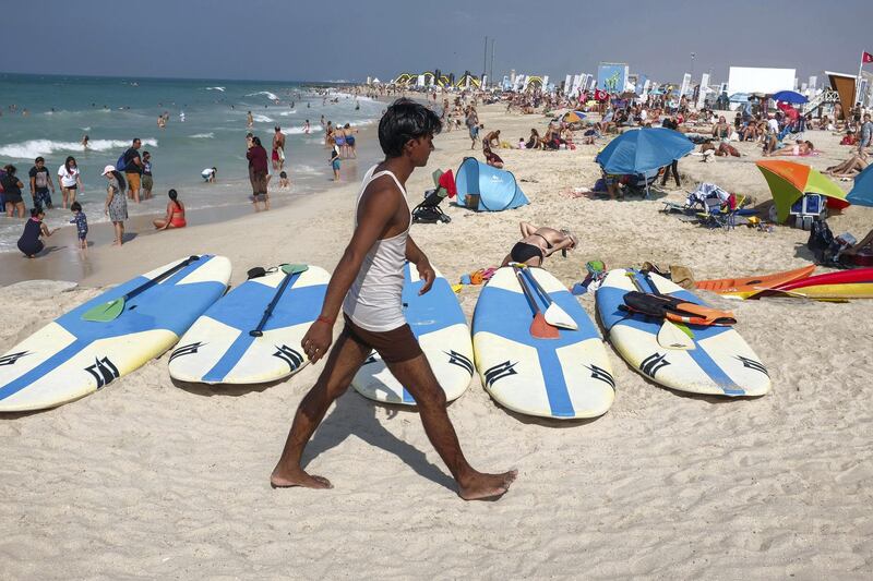 DUBAI, UNITED ARAB EMIRATES. 18 NOVEMBER 2018. Residents and visitors to Dubai enjoy the public holiday on the birthday of Prophet Mohammad (PBUH), also known as Eid Al Mawlid an Nabawi, in the sunshine on Kite Surf Beach. Beach goeres woalk past Stand Up Paddle boards that are for rent at the beach. (Photo: Antonie Robertson/The National) Journalist: None. Section: National.