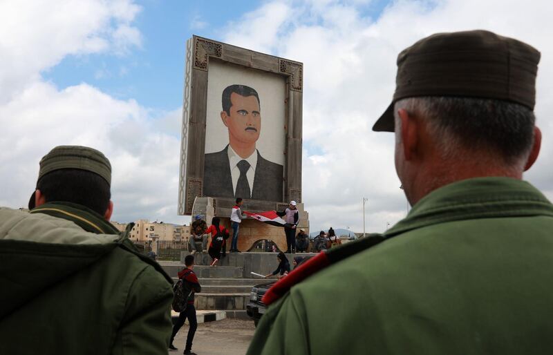 Protesters hold national flags under a a giant portrait of Syrian President Bashar al-Assad in Quneitra in the Syrian Golan Heights. AFP