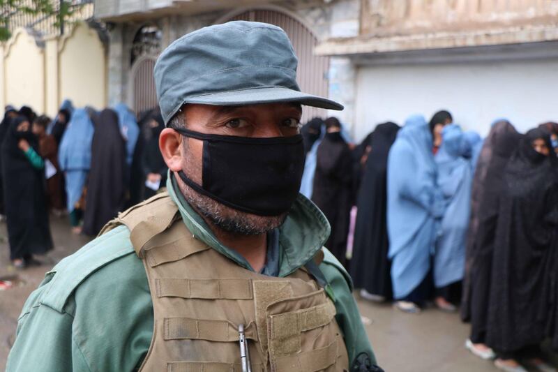 A security force member stands guard as women line up to receive rations distributed by the World Food Programme in Herat, Afghanistan, 31 March. Jalil Rezayee / EPA