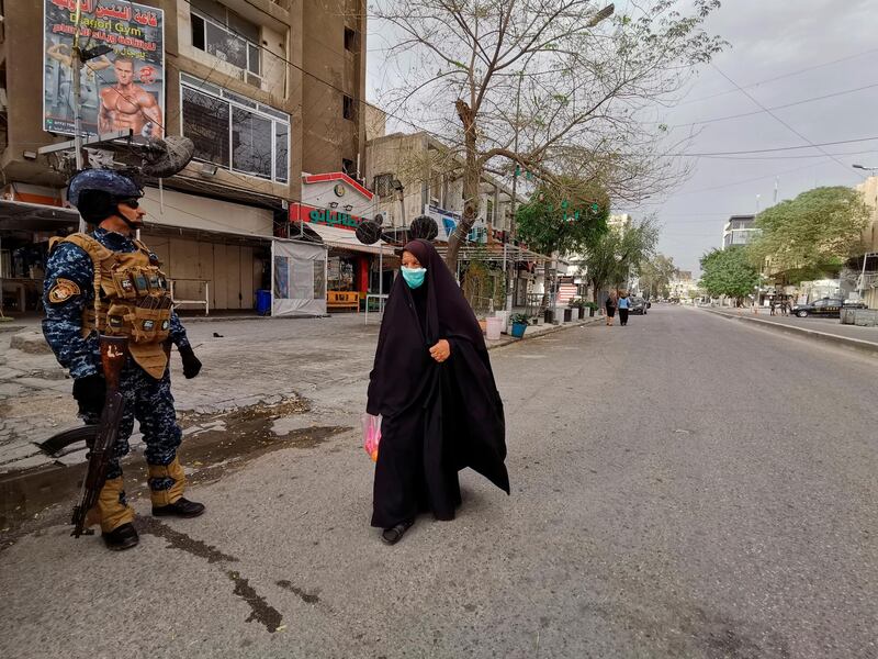 A federal policeman stands guard while people walk in a nearly empty street during a curfew to help fight the spread of the coronavirus. in central Baghdad, Iraq. AP Photo
