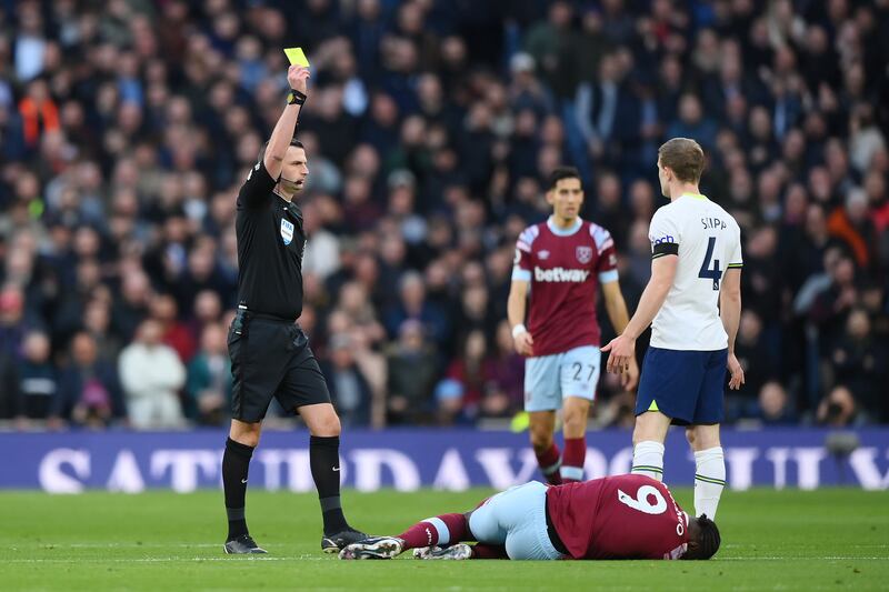Referee Michael Oliver shows a yellow card to Oliver Skipp of Tottenham as Michail Antonio of West Ham United lies injured. Getty