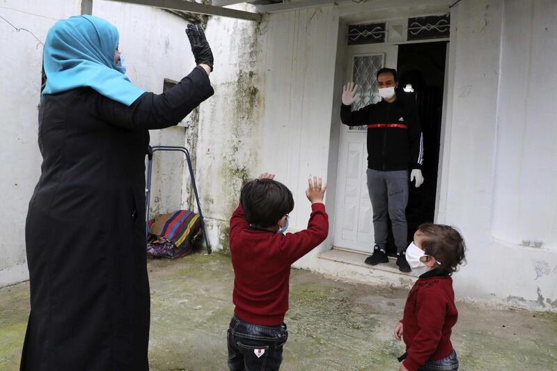 Islam Bseileh, a 29-year-old Palestinian who used to work in Israel, waves to his wife and two kids (all wearing masks) as he receives food they delivered to him while in quarantine in his home in the city of Hebron in the occupied West Bank.   AFP