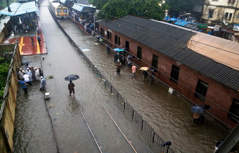 FILE - In this Tuesday, Aug. 29, 2017 file photo, people walk past a waterlogged railway station during heavy rainfall in Mumbai, India. Two massive, rain-soaked cities on opposite sides of the world are struggling with swirling, brackish waters that have brought death and devastation. For Houston, itâ€™s unprecedented. For Mumbai, itâ€™s painfully common. India's financial capital was especially hard hit, with water swamping offices, schools and roads and about 60 people killed, 33 alone in Thursdayâ€™s collapse of a 117-year-old apartment building whose foundation had been weakened by the flooding. (AP Photo/Rajanish Kakade, File)