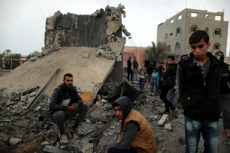 Palestinians sit at the remains of a building. Reuters