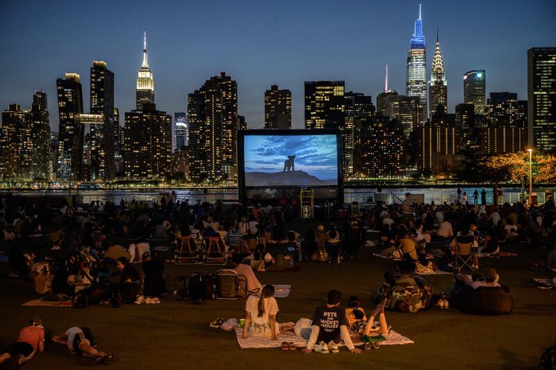 People sit in a public park to watch an outdoor screening of 'The Lion King' before the Manhattan skyline in Long Island City, in New York.