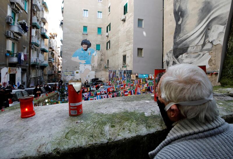 A man wearing a protective face mask stands in front of a mural depicting Diego Maradona, as people gather to mourn his death in Naples. Reuters