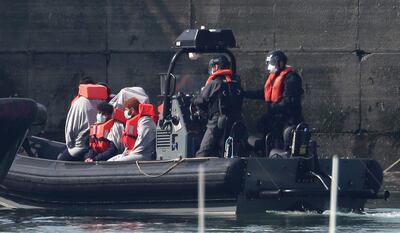 Border Force officers with men thought to be migrants, wearing face masks as they come to shore in Dover, south England, after what has been described as a small boat incident in The Channel early Thursday May 7, 2020.  The highly contagious COVID-19 coronavirus has impacted on nations around the globe, many imposing self isolation and exercising social distancing when people move from their homes. (Gareth Fuller / PA via AP)