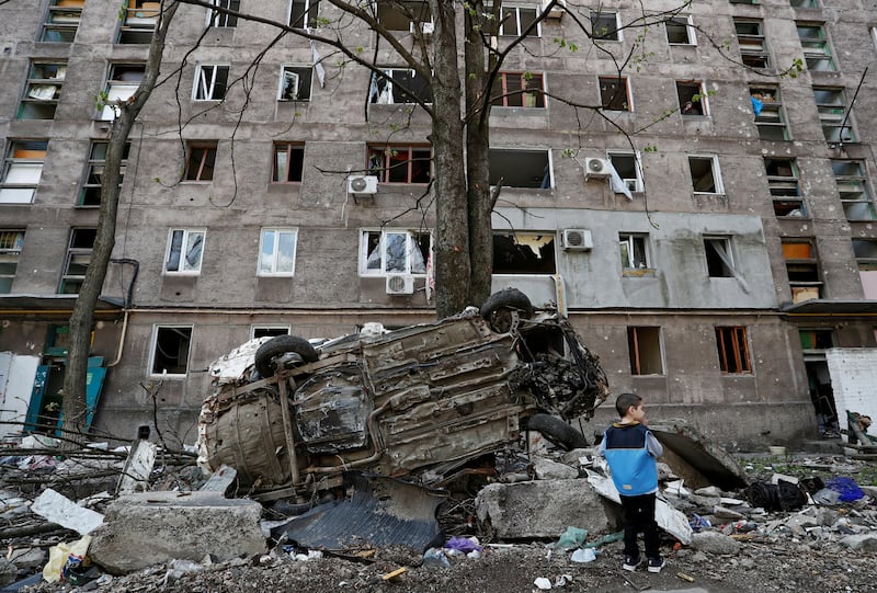 A boy stands next to a wrecked vehicle in front of an apartment damaged during the conflict in the southern port city of Mariupol. Reuters