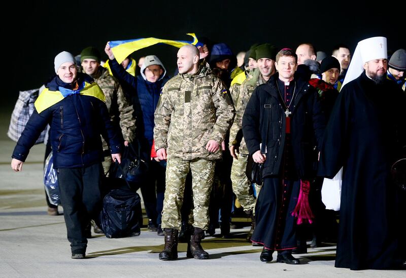 Prisoners who were released by separatists, with the national flags, smile, accompanied by clerics and officials leave the plane after landing in Kiev Boryspil Airport, Ukraine, early Thursday, Dec. 28, 2017. Ukrainian authorities and Russian-backed separatist rebels on Wednesday conducted the biggest exchange of prisoners since the start of an armed conflict in the country's east and a sign of progress in the implementation of a 2015 peace deal. (AP Photo/Efrem Lukatsky)