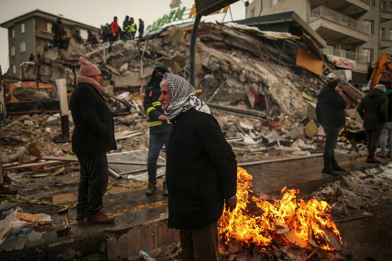 People warm themselves next to a collapsed building in Malatya, Turkey, on February 7. AP