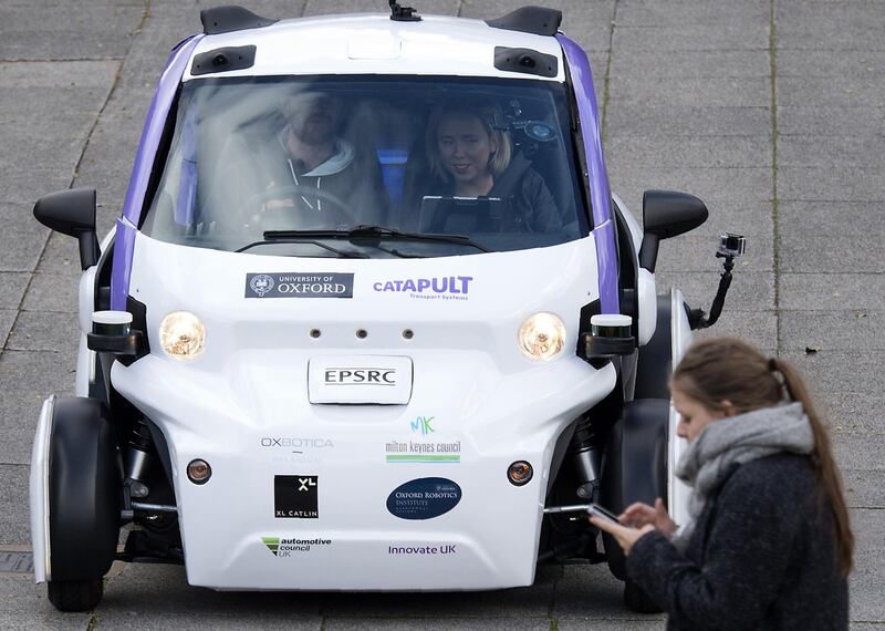 A woman uses a mobile phone as she walks in front of an autonomous self-driving vehicle, as it is tested in a pedestrianised zone, during a media event in Milton Keynes, north of London, on October 11, 2016. - Driverless vehicles carrying passengers took to Britain's streets for the first time on Tuesday in a landmark trial which could pave the way for their introduction across the country. The compact two-seater cars trundled along a pedestrianised zone in Milton Keynes, north of London, in a trial by Transport Systems Catapult (TSC) which plans to roll out 40 vehicles in the city. (Photo by JUSTIN TALLIS / AFP)