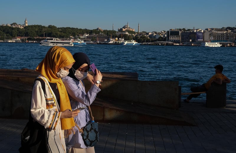 Women wearing face masks check their phone as they walk with the Hagia Sophia Mosque seen in the background, in Istanbul, Turkey.  EPA