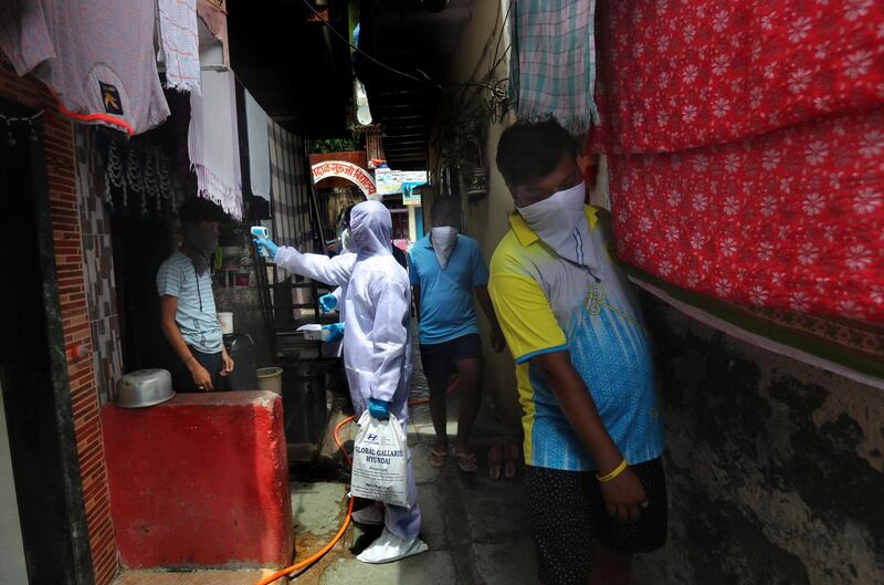 A health worker checks the temperature of a boy as people walk past in a narrow lane during a free medical check-up in a slum in Mumbai. AP