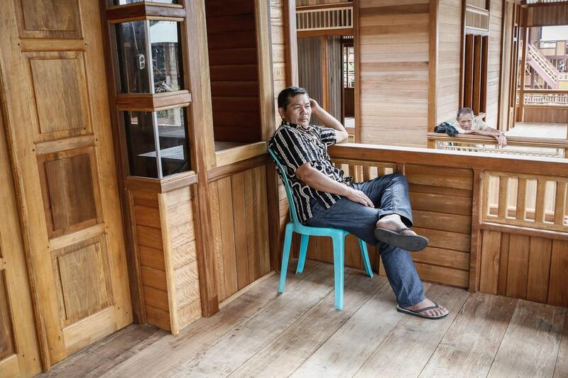 A constructor awaits customers on the porch of a newly built wooden house. Putu Sayoga / Getty Images
