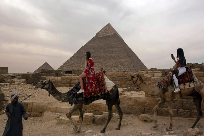 In this Tuesday, March 10, 2020, photo, two foreign women tourists ride camels at the Giza Pyramids near Cairo, Egypt. The country's prime minister announced at a news conference on Tuesday, March 24, 2020, a two-week, 7 p.m. to 6 a.m. curfew for its over 100 million people to slow the spread of the new coronavirus. The 11-hour curfew would go into effect Wednesday across the country and last for two weeks. (AP Photo/Maya Alleruzzo)