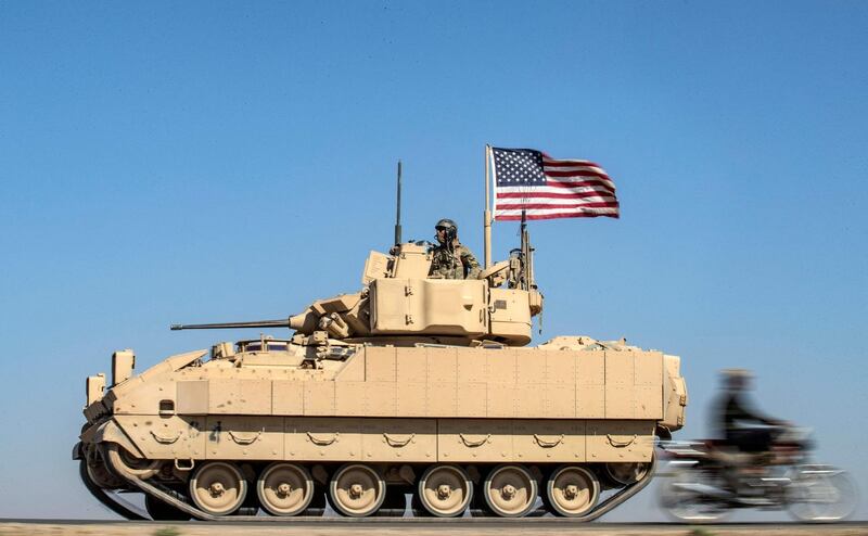 A motorcycle passes a US Bradley Fighting Vehicle flying the US flag near oil wells at Rmelan. Despite scaling down its presence in Syria, the US has retained personnel in Hasakeh. AFP