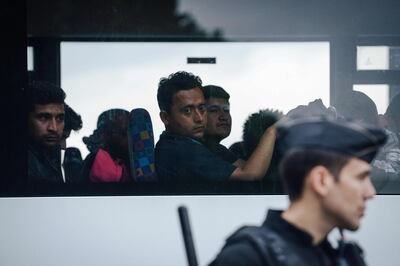 TOPSHOT - An anti-riot policeman stands guard in front of migrants sit aboard a bus after being evicted by French police from a makeshift camp along the Canal de Saint-Martin at Quai de Valmy in Paris, on June 4, 2018. More than 500 migrants and refugees were evacuated on early June 4, 2018 from a makeshift camp that had been set up for several weeks along the Canal. / AFP / Lucas BARIOULET

