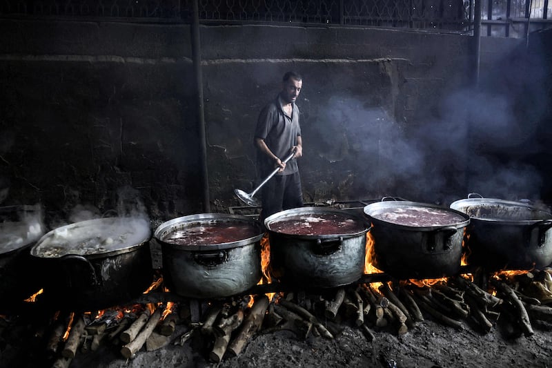 A Palestinian man stirs one of several large cooking pots simmering on wooden fires due to the lack of cooking gas. AFP