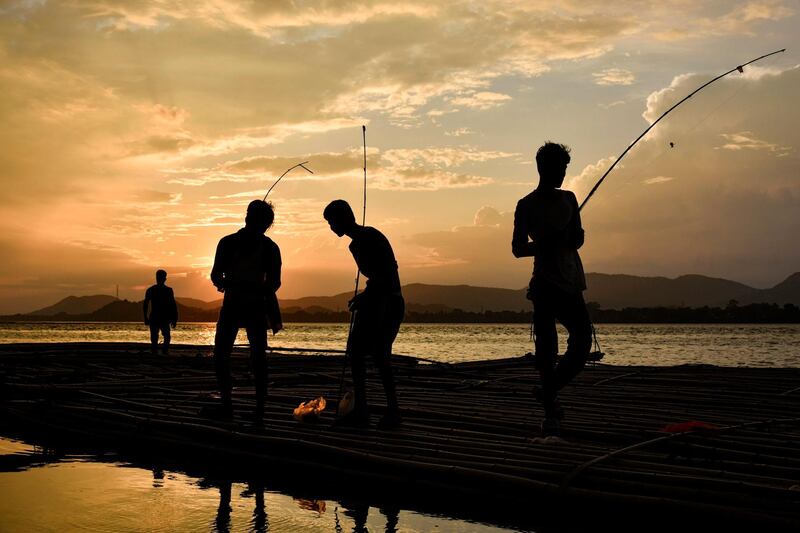 Indian youths fish at sunset on floating bamboo along the Brahmaputra river in Guwahati, Assam.  AFP