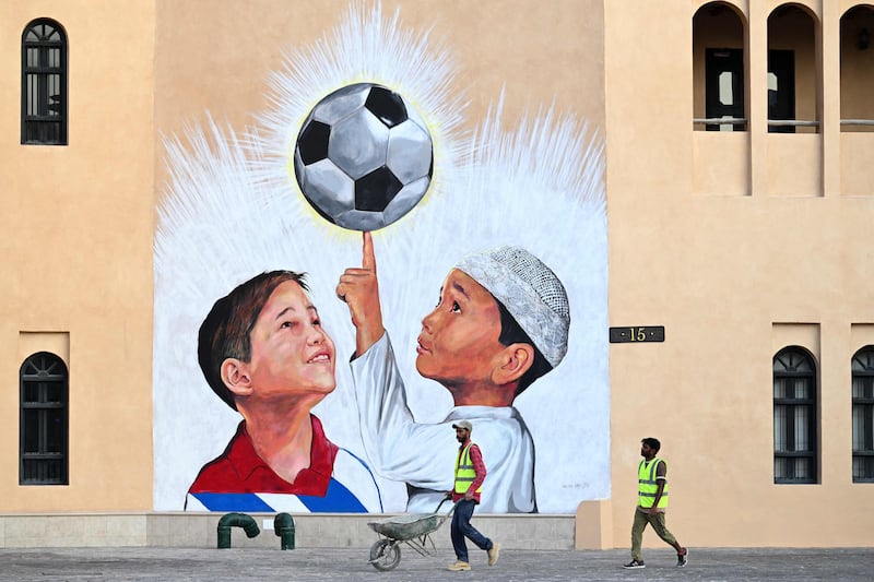 A worker pushes a wheelbarrow past a mural in Doha. AFP