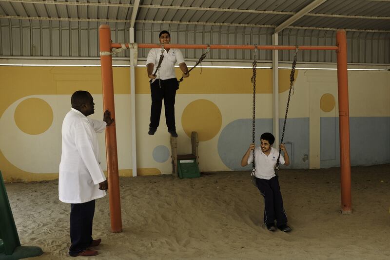 Teenagers play on the swings at the Dubai Autism Centre, watched over by the centre’s Prof Honest Ncube. Sheikh Hamdan’s donated Dh22million towards the centre.  Jaime Puebla / The National