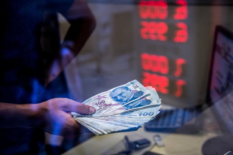 A teller holds Turkish lira banknotes at a currency exchange office in Istanbul on August 13, 2018. - Turkey's troubled lira tumbled on August 13 to fresh record lows against the euro and dollar, piling pressure on stock markets on fears the country's crisis could spill over into the world economy. (Photo by Yasin AKGUL / AFP)