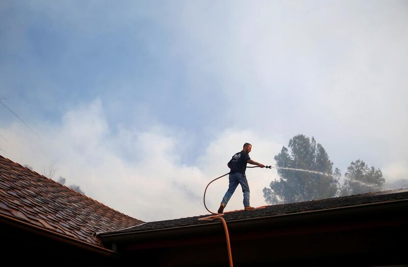 A resident sprays down a roof as firefighters battle the Peak fire in Simi Valley. Reuters