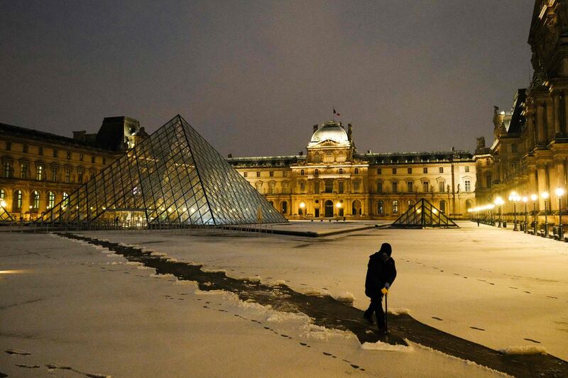 An employee clears snow at the Louvre in Paris, with the Louvre Pyramid, designed by Chinese-American architect Ieoh Ming Pei, in the background. AFP