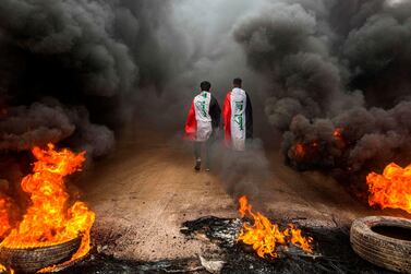 Anti-government protesters draped in Iraqi national flags walk into clouds of smoke from burning tyres during a demonstration in the southern city of Basra on November 17, 2019. AFP