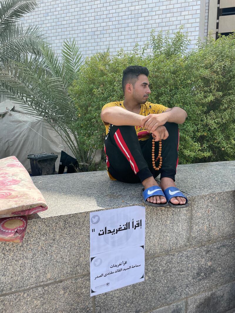 A protester sits outside the parliament next to an announcement that urges followers of Mr Al Sadr to follow his statements on Twitter. 