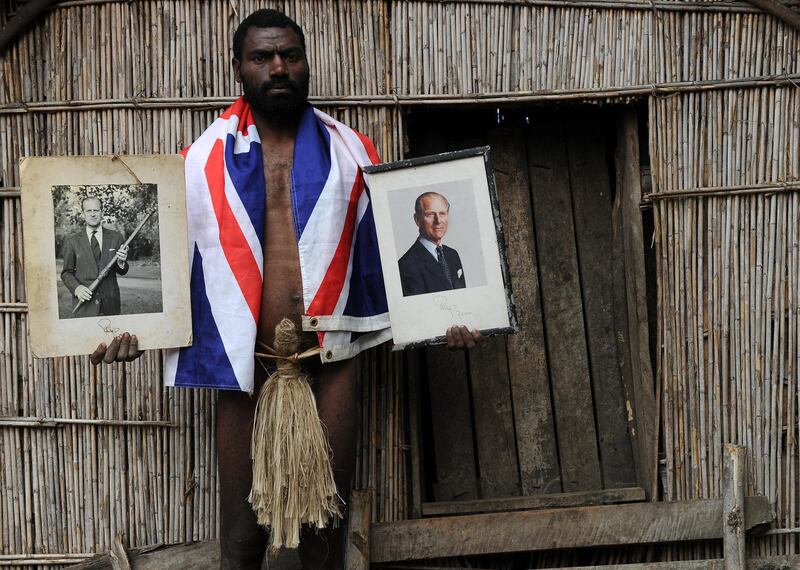 TO GO WITH AFP STORY "Vanuatu-Britain-religion-royals,FEATURE" by Madeleine Coorey
Sikor Natuan, the son of the local chief, holds two official portraits (one holding a pig-killing club, L) of Britain's Prince Philip in front of the chief's hut in the remote village of Yaohnanen on Tanna in Vanuatu on August 6, 2010. In his remote village in Vanuatu, tribesman Sikor Natuan cradles a faded portrait of Britain's Prince Philip against his naked and tattooed chest. Natuan, who just weeks before danced and feasted to mark the royal's 89th birthday, is already preparing for next year's celebrations -- and he is expecting the guest of honour to attend, despite his advanced age. For in the South Pacific village of Yaohnanen on Vanuatu's Tanna island, where men wear nothing but grass penis sheaths, and marijuana and tobacco grow wild, Prince Philip is worshipped as a god.  AFP PHOTO / Torsten BLACKWOOD (Photo by TORSTEN BLACKWOOD / AFP)
