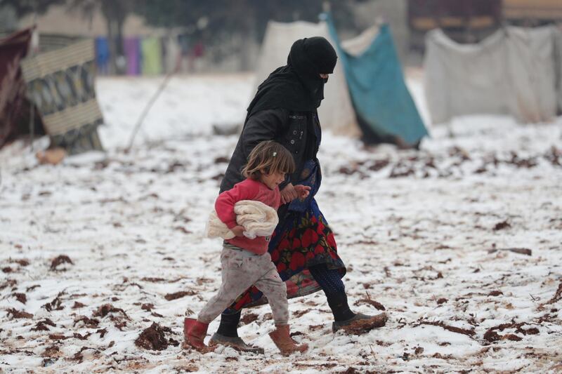 An internally displaced woman holds the hand of a child carrying bread, as they walk on snow at a makeshift camp in Azaz, Syria. REUTERS