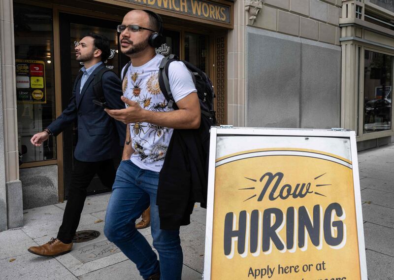 People walk past a restaurant with a hiring sign in Washington. In the US, there are indications that the labour market is slowing and wage pressures are easing. AFP
