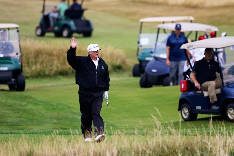 U.S. President Donald Trump waves to protesters while playing golf at Turnberry golf club, in Turnberry,  Scotland, Saturday, July 14, 2018. A dozen demonstrators have staged a protest picnic on the beach in front of the Trump Turnberry golf resort in Scotland where President Donald Trump is spending the weekend with the first lady. (AP Photo/Peter Morrison)