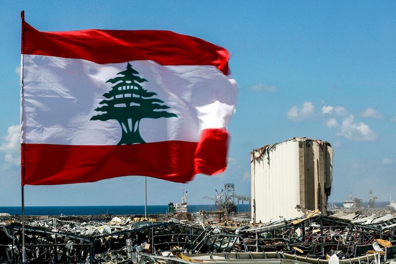 This picture taken on August 9, 2020 shows a Lebanese flag flying along a bridge near the port of Lebanon's capital Beirut, while in the background are seen the damaged grain silos opposite the blast site of a colossal explosion due to a huge pile of ammonium nitrate that had languished for years at a port warehouse. The huge chemical explosion that hit Beirut's port, devastating large parts of the Lebanese capital and claiming over 150 lives, left a 43-metre (141 foot) deep crater, a security official said. The blast Tuesday, which was felt across the country and as far as the island of Cyprus, was recorded by the sensors of the American Institute of Geophysics (USGS) as having the power of a magnitude 3.3 earthquake. / AFP / JOSEPH EID
