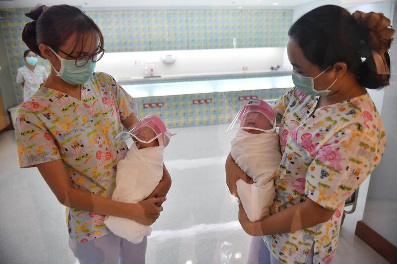 This photo taken through a glass window at a maternity ward shows nurses holding newborn babies wearing face shields, in an effort to halt the spread of the COVID-19 coronavirus, at Praram 9 Hospital in Bangkok on April 9, 2020. (Photo by Lillian SUWANRUMPHA / AFP)