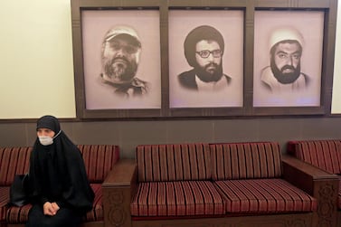 A mask-clad woman sits next to portraits of late Hezbollah leader Abbas Mussawi, late commanders Imad Mughnieh and Ragheb Harb, at a Hezbollah centre in Beirut's southern suburbs. AFP 