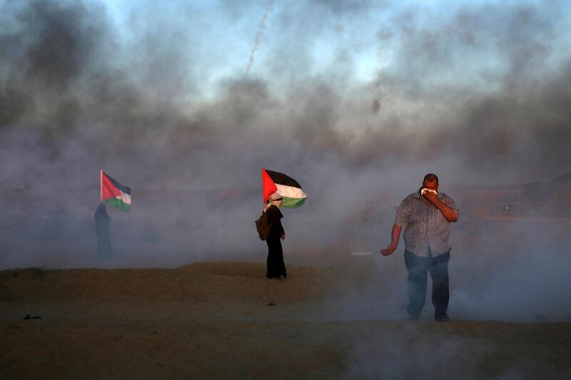 A protester covers his face to protect from teargas fired by Israeli troops while others wave their national flags near the fence of the Gaza Strip border with Israel during the protest. AP Photo