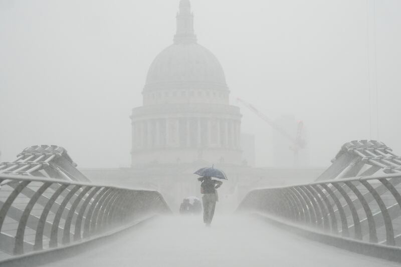 Pedestrians brave the downpour to cross Millennium Bridge in London, with St Paul's Cathedral almost obscured by the rain. PA