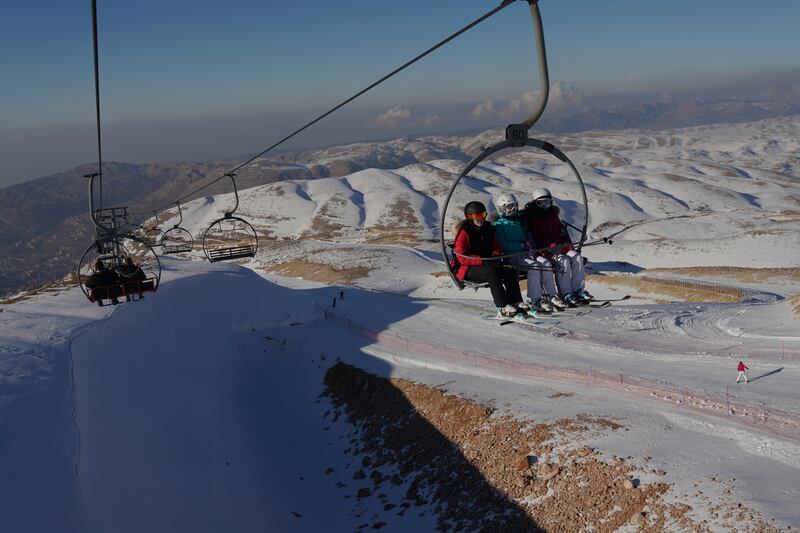 Skiers travel by chair lift, with the Mediterranean Sea in the background.