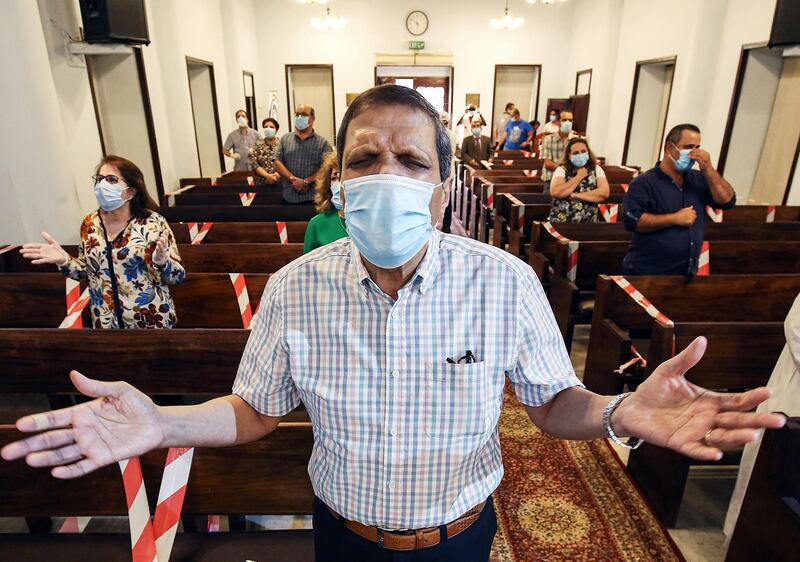 Mask-clad worshippers, adequately distanced from each other, sing together a prayer song during a service at the National Evangelical Church in Kuwait City.  AFP